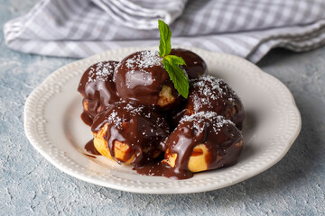 Delicious profiteroles with chocolate and white plate. Selective focus image on light background.