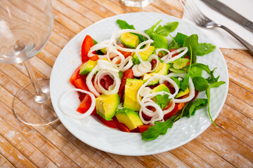Colorful salad with fresh ripe tomatoes, green ripe avocado, sliced onion and herbs. Vegetarian appetizer