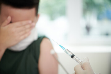 Scared boy covering eyes with hand when doctor showing syringe with vaccine against coronavirus