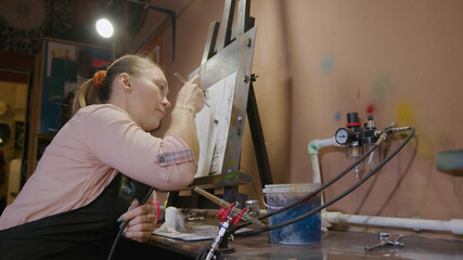 Woman artist learns to paint with airbrush with acrylic dye, paper and easel. Concept modern art,...