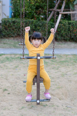 .A cute little Asian girl playing on a rocking horse and raising her hands in joy.