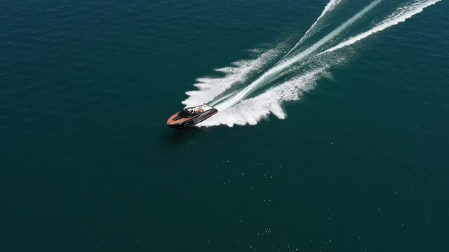 Luxury boat in dark color, fast movement on blue water, aerial view. Expensive luxury Italian boat moving on the water top view. Boat dark wood, movement on the water top view.