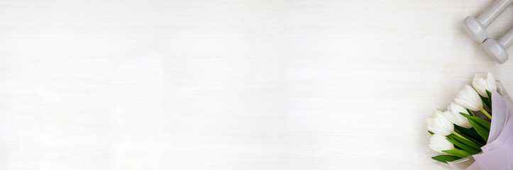 Two white dumbbells and tulips on white background with copyspace. Healthy fitness lifestyle flat lay banner composition for Valentine's Day, birthday, anniversary or wedding.