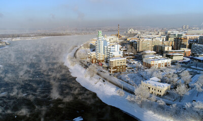 The old bridge over the Angara river. Steam is emitted from the water. Aerial drone flight. In winter, the Russian city is covered with ice and snow.