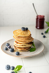 sweet pancakes for breakfast in a stack. on a ceramic plate. with fresh blueberries and mint. light key vertical position