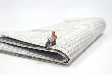 a figure of a man reading a newspaper while sitting on a full size newspaper