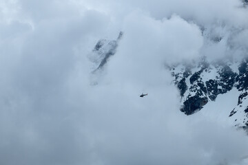 A helicopter crosses the clouds towards the Aiguille du Midi and the Bossons glacier in the Mont Blanc massif in Europe, France, the Alps, towards Chamonix, in summer.