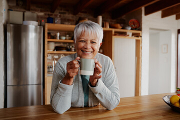 Portrait of retired biracial elderly female leaning on kitchen counter smiling at camera. Happy pensioner