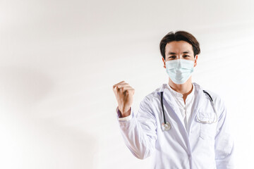 A Young Asian male doctor intern with a stethoscope, surgery face mask in medical coat excited, glad man raised arms in a hospital office. Positive, confident Healthcare and medicine concept ideas