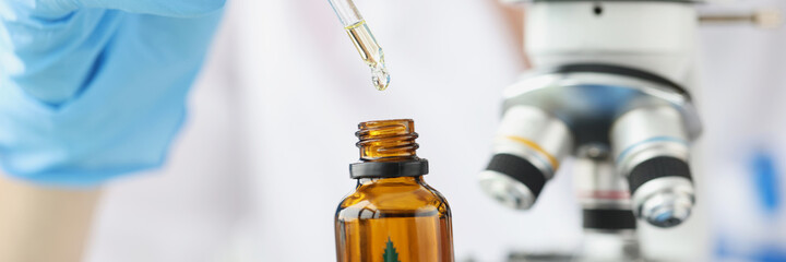 Scientist chemist examining marijuana oil under microscope in lab clo
