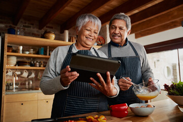 Low angle of Multi-cultural elderly couple smiling, using tablet to research recipe in modern kitchen. 