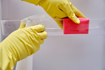 Cleaning the refrigerator from dirt, a man hand in yellow gloves wipes kitchen appliances