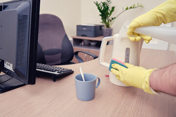 Cleaning of kitchen appliances in the office, male hand in yellow gloves wipes the kettle with a sponge