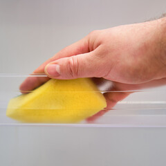 A man hand with a yellow sponge washes the refrigerator