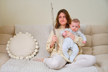 Problems with rehearsals and music lessons after childbirth. Sad woman mom with infant baby and flute on home sofa © Андрей Журавлев