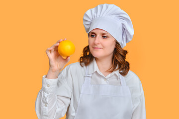 Happy woman chef with orange fruit in hands on studio background, copy space