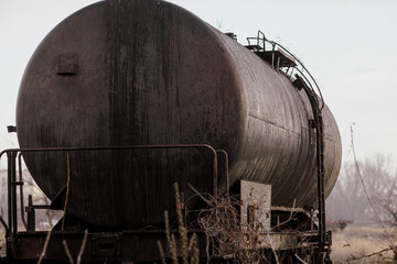 Shallow depth of field (selective focus) image with old and rusty railway oil tanker in the middle of a field on a sunny winter day.