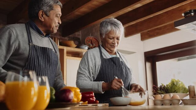 Multi-cultural elderly couple cooking together in modern kitchen. Smiling, happily retired partners