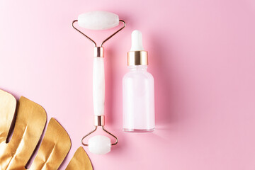 Skin care concept. Bottle of cometic product, serum or oil. Quartz roller for face massage. Cosmetics and tools on pink background with copy sapce.