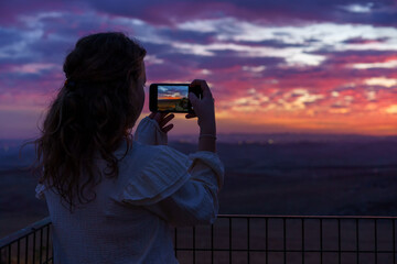 Back view beautiful little girl takes a picture of the amazing sunset.