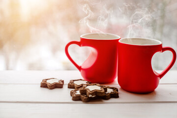 two heart shaped mugs with tea on the background of a window in winter
