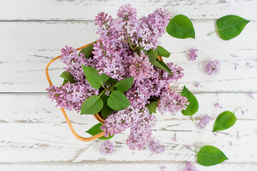 top view of the spring bouquet of purple lilacs in a flower basket on a white wooden background. spring composition to create a good mood.