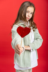 portrait of a beautiful girl in a green denim jacket and a white shirt and loose hair. on a red background. close-up. heart on a stick. Valentine's Day. red candy