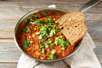 Homemade vegetarian stew with beans, vegetables and cilantro in a frying pan on a gray wooden culinary background close-up	