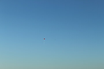 Fototapeta na wymiar Red balloon in flight. Photo taken on the road in ören burhaniye aegean sea coast turkey anatolia asia. Fresh air calm warm open weather day in summer 2021.