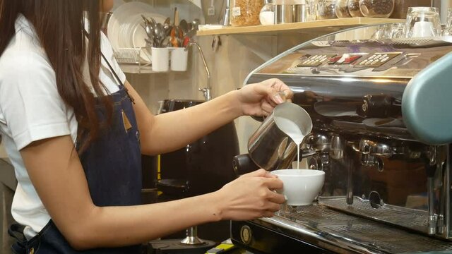 4K. professional barista making a cup of coffee. bartender pouring milk foam in front of coffee maker machine, preparing latte art hot coffee for serving customer at coffee shop cafe