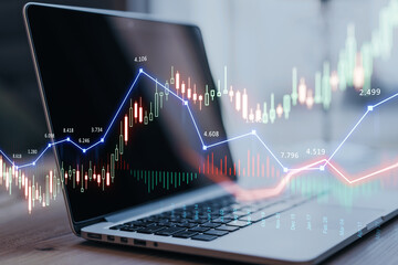 Close up of laptop computer on desktop with glowing forex chart trading interface on blurry...