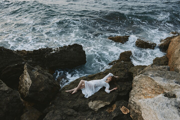 Beautiful bride lying on rocky coast with cracks on rocky surface unaltered