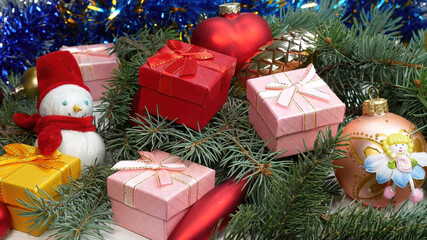 5 Christmas gifts in pink, yellow and red, along with Christmas decorations, a snowman, and a bauble fairy, in a pile of pine branches.