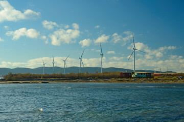 Wind turbine on the mediterranean sea with fishermen shacks. Wind farm near Piombino, Tuscany, Italy, with clouds and sea