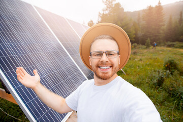 Happy Scandinavian man in hat and glasses takes selfie photo background of solar panels. Concept friendly technology for environment