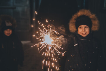 boy holds a sparkler in his hands while celebrating a new year on the street at night. Fireworks in...