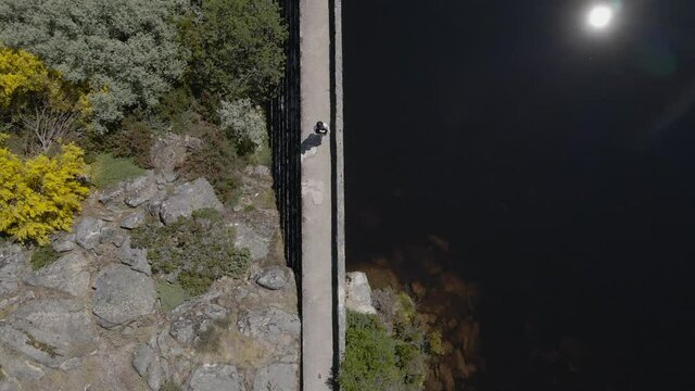 A person walks across a bridge over dark water of Cov&atilde;o dos Conchos in the Serra da Estrela Mountains 