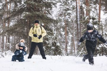Father and sons having fun snowball fight together in winter forest. Happy children playing in snow outdoors. Christmas holidays, New year family vacation. Brothers in warm clothes walking in cold day