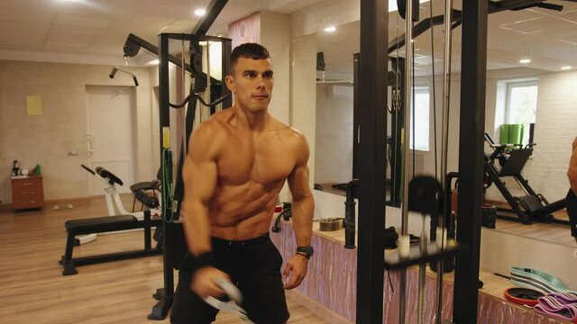 A young man training in the gym and does a straight arm lift on a crossover simulator for pumping deltoid muscles