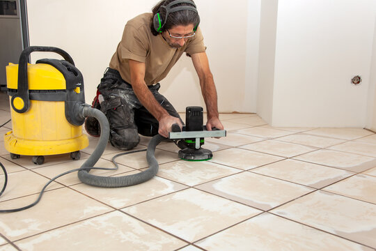 Man is working with a Grinder. Tiles floor surface grinding by electric flooring grinding machine for a smooth base. Preparation for an even floor to installing a new thin vinyl as a floor covering 