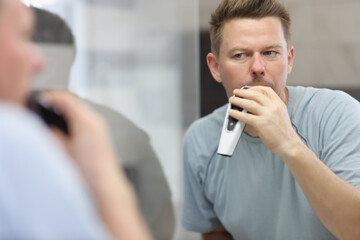 Middle aged man shaving beard with machine early in morning