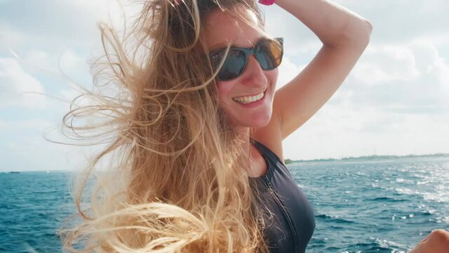 Woman in tropics. Portrait of the young woman relaxing on roof of the boat moving in the tropical sea. Woman with long hair enjoys the wind and looks in the camera and smiles