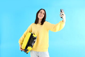 Woman with travel bag doing selfie on blue background