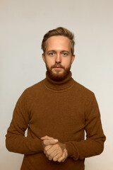 Astonished Caucasian young male standing against white studio wall keeping fingers interlocked in front of him looking at camera with surprise and puzzlement in his beautiful blue eyes