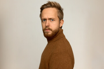 Studio shot of attractive stylish brutal manful man standing half-turned to camera with suspicious doubtful face expression, trying to guess what's going on around, isolated on white