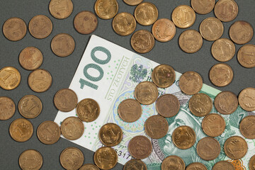 PLN 100 bill and one-grosz coins on a dark grey background.