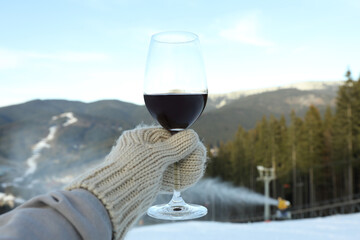 Hand in mitten holds glass of wine against mountains