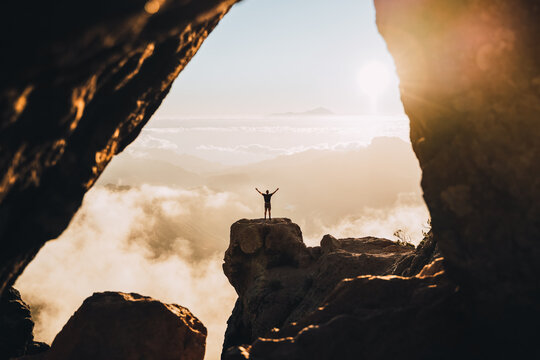 man on the top of a cliff during the sunset with raised hands