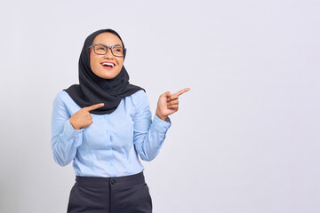 Portrait of smiling young Asian woman pointing finger at copy space isolated on white background