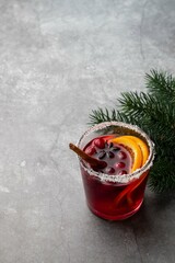 Hot mulled wine for winter with cranberry, spices, cinnamon and orange slices in glass cup on grey...